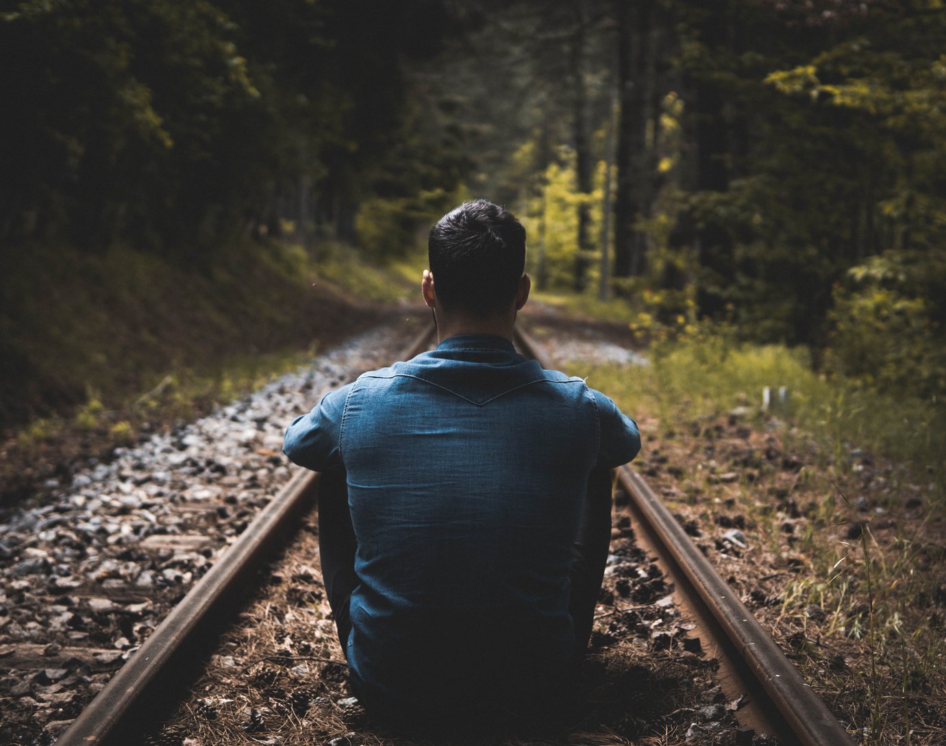 Man Sitting on Rail Track Selective Focus Photography